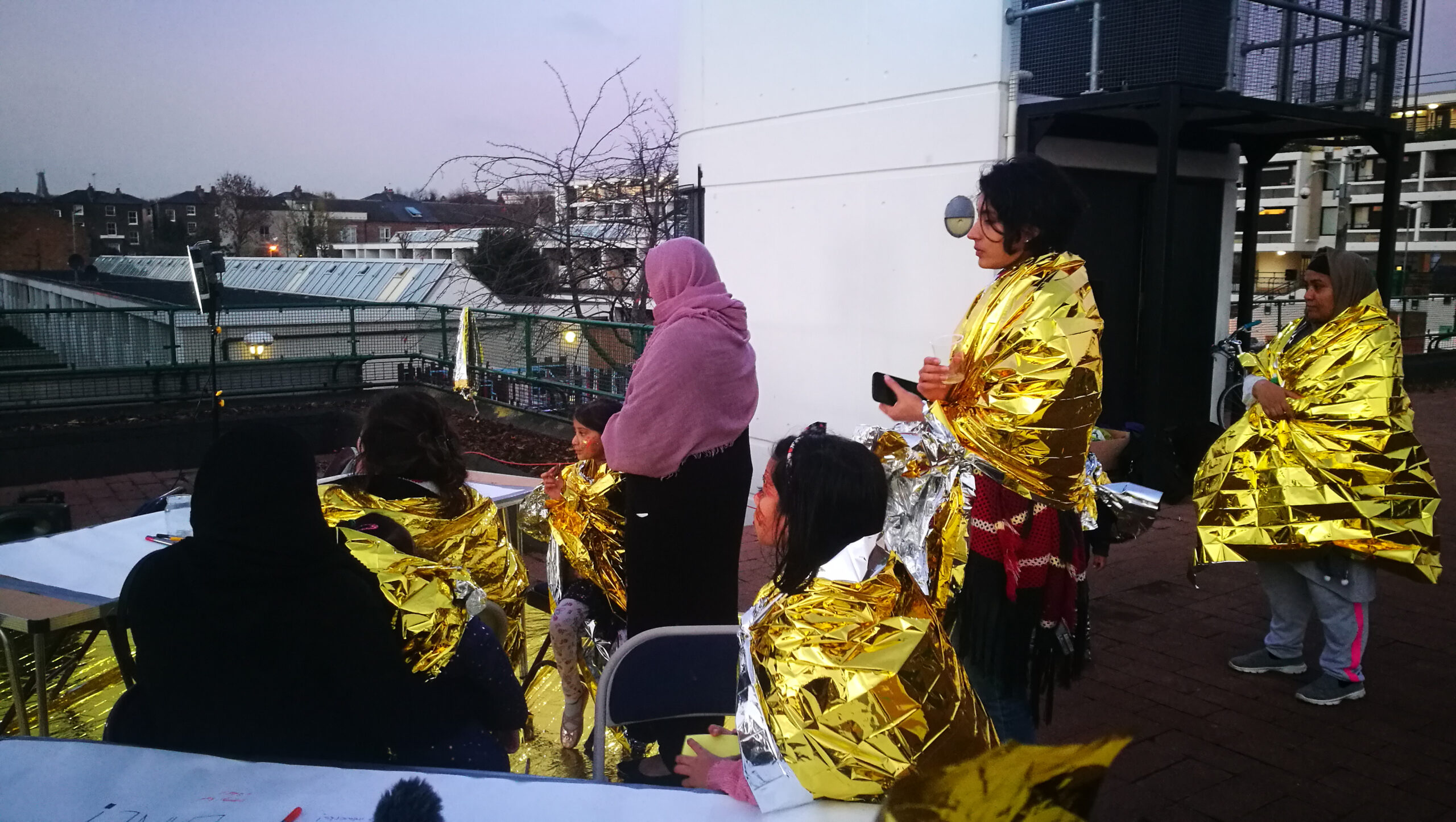 photograph of women in gold heat blankets participating in an activity on a rooftop