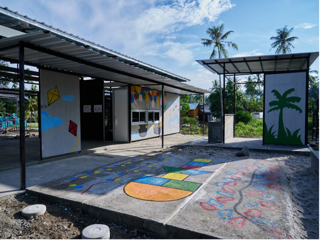 Image showing modular school building made of black metal framework with corrugated grooves and pale grey wall panels, that are part of the Sekolah Indonesia Cepat Tanggap quick response school design.  