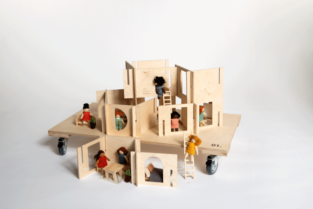 Buildable wooden toy houses with miniature furniture and felt dolls on a plywood dolly.